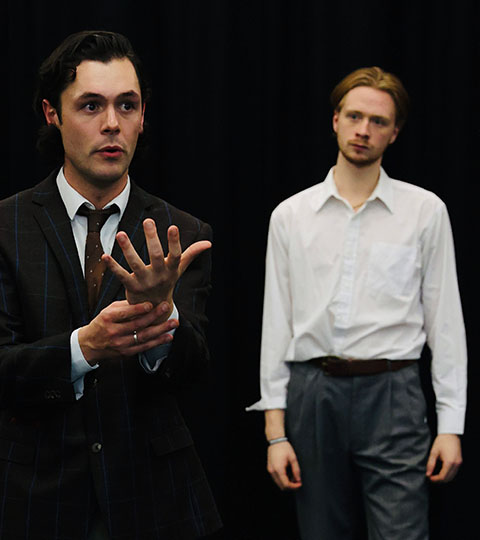 Two men, one in a suit, one in a white shirt standing against a black background