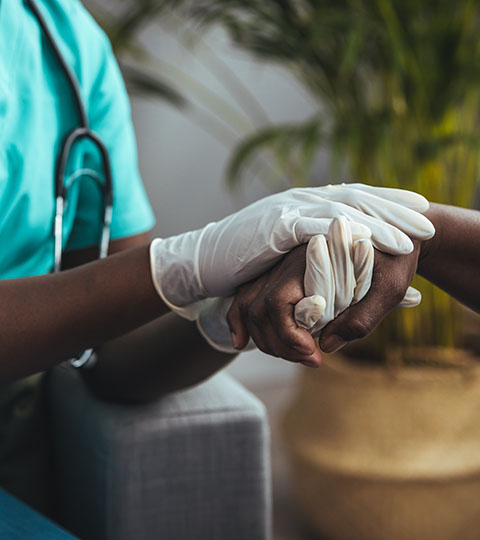 A nurse's gloved hands holding a patient's hand