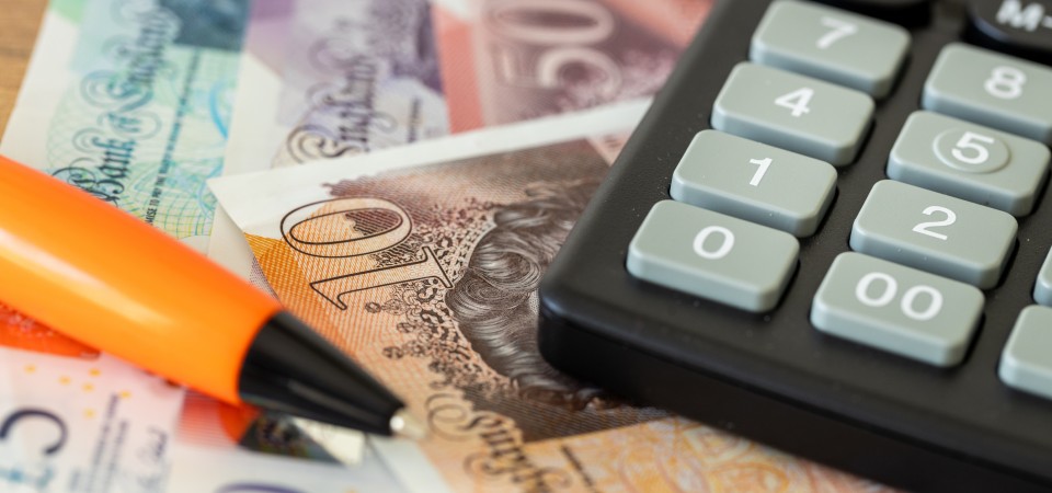 a pen and calculator on top of ten pound notes