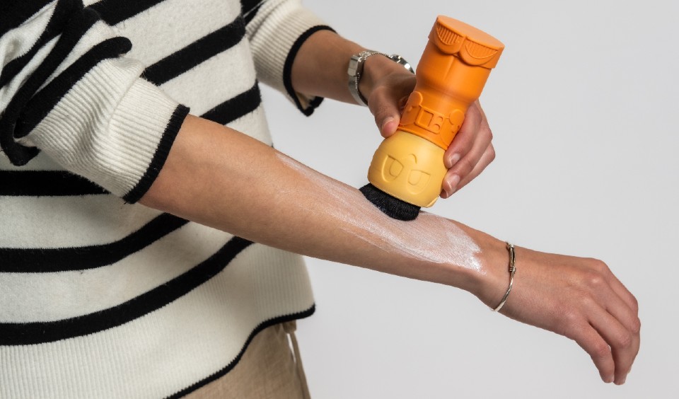 A woman applying suncream to her arm using the astronaut-shaped Sunny applicator