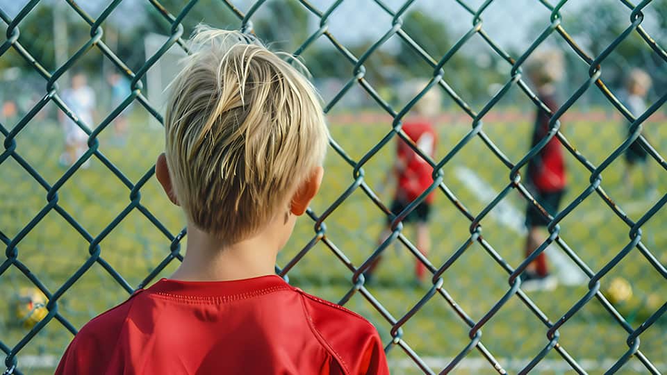 A child looking through a wire fence onto a football pitch