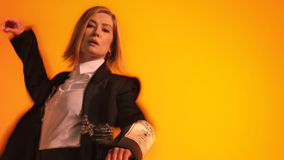 A woman against a yellow backdrop, dancing and looking at the camera.