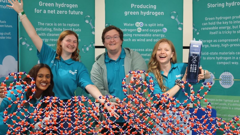 Four people stood behind of a 3D model of molecules smiling for a photo.