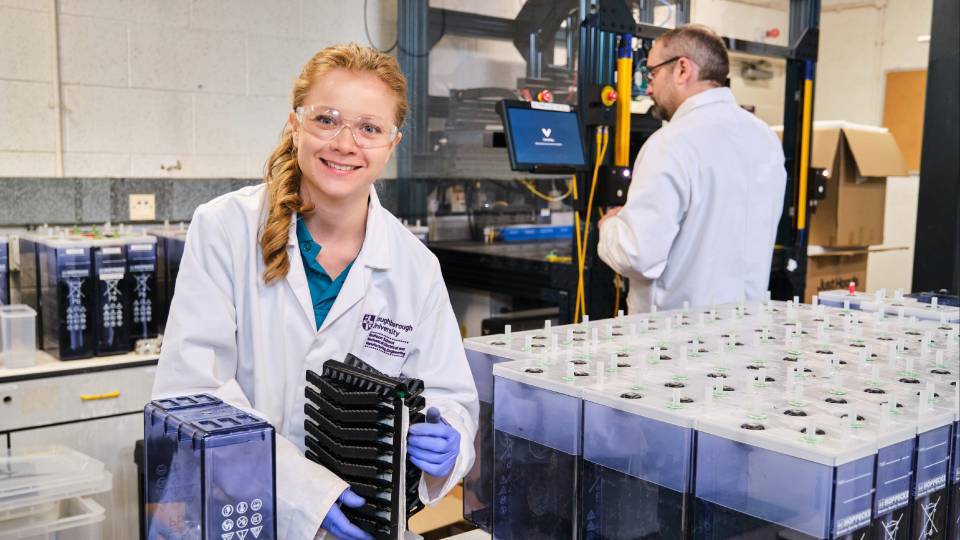 Two people in a lab wearing white lab coats and gloves, working with scientific equipment.
