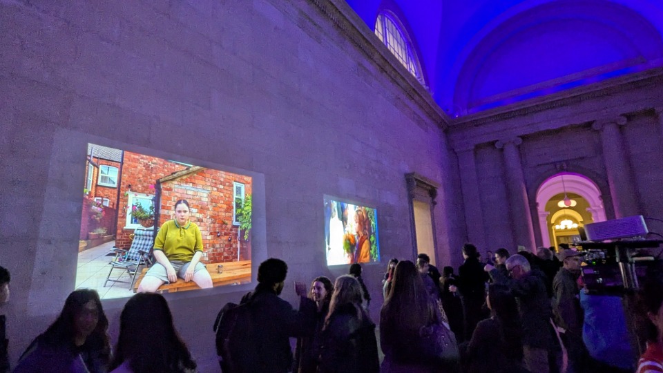 The Duveen hall in Tate Britain with projected images on the brick walls. People networking and looking at the projections