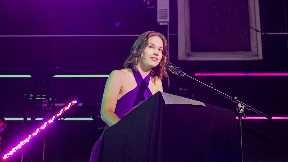Daisy Newton standing on stage speaking into a microphone.