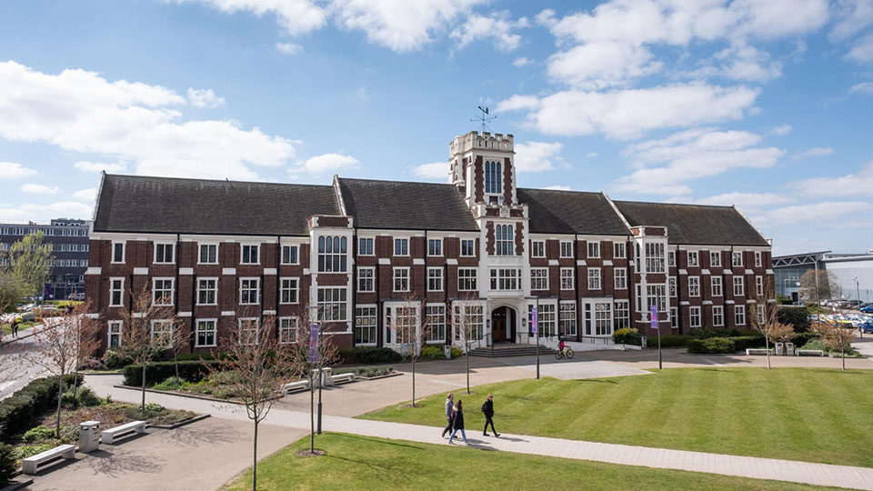 Side view of Hazlerigg Building on a sunny day, with the Hazelrigg-Rutland lawn shown in front and people walking around