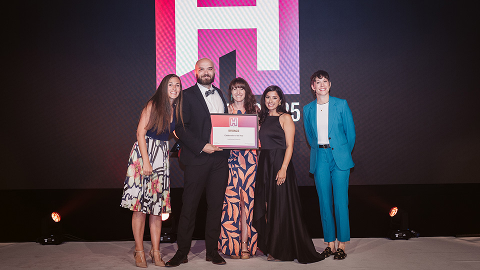 Five people standing on stage holding a certificate at the HEIST Awards ceremony.