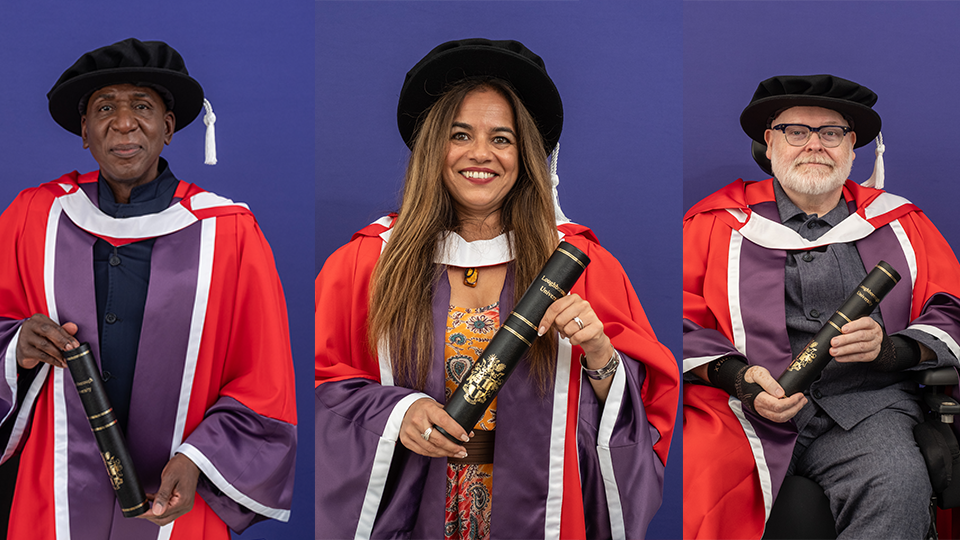 Three honorary graduates holding scrolls and wearing formal graduation wear in front of a purple wall