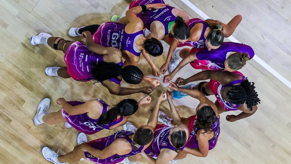 an aerial shot of lightning netball players in a huddle