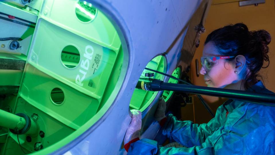 A woman wearing a lab coat and glasses looking into a machine