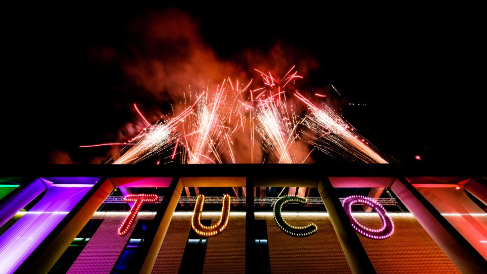 Fireworks shooting into the sky above a lit up sign reading 'TUCO'.
