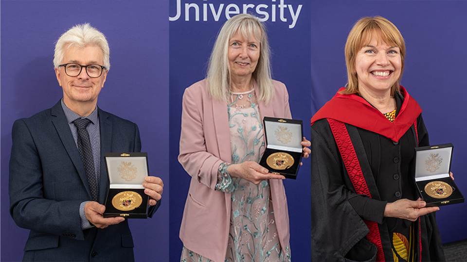 Three recipients of the University Medal, stood smiling at the camera holding their medal in front of a purple wall