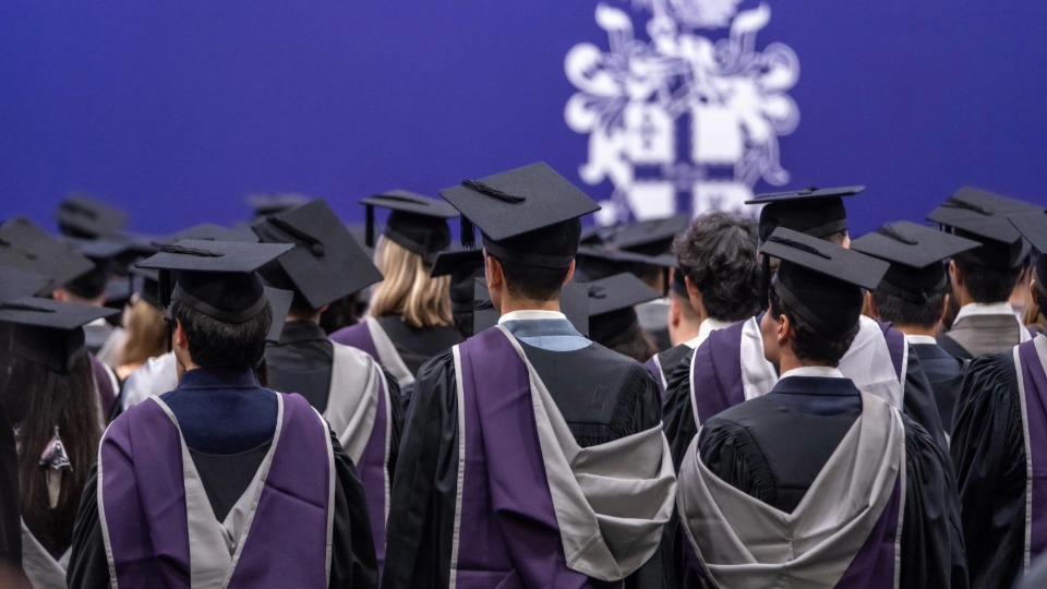 Students at graduation sat facing a purple wall with a Loughborough crest