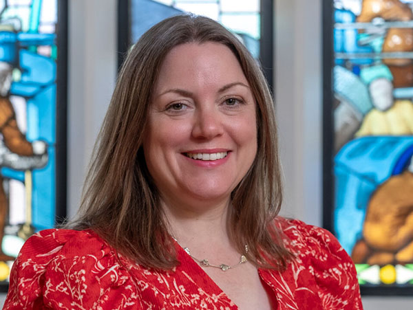 Headshot of Kathryn in front of a stained glass window with a red top on