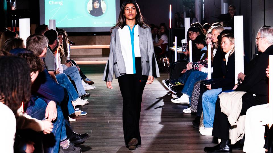A model walking down a catwalk wearing a grey blazer.