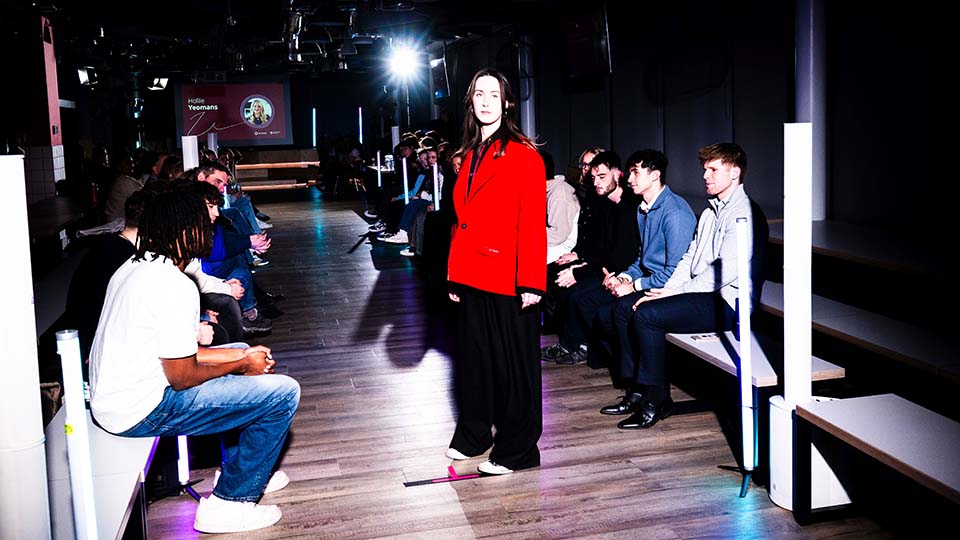 A model standing at the end of a catwalk wearing a red blazer.