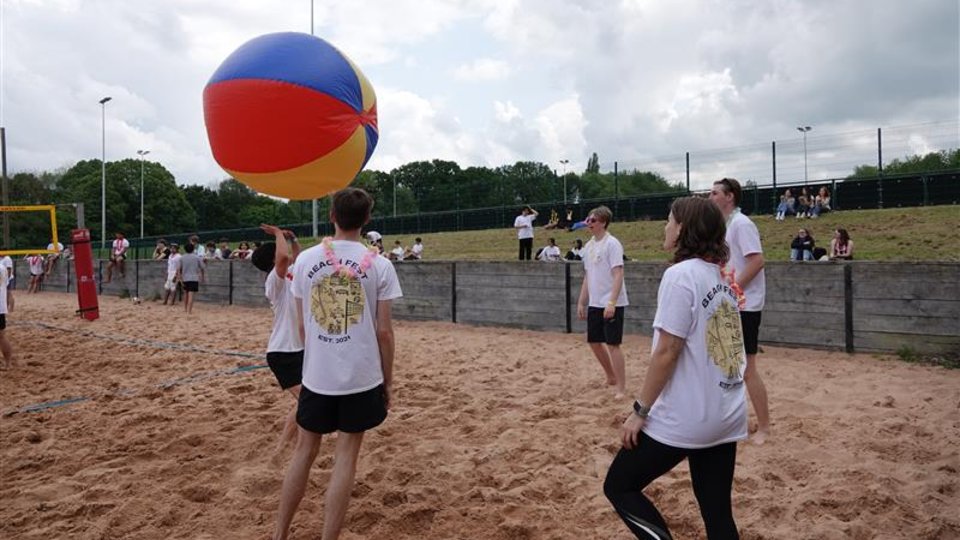 A group of people playing volleyball on a sandy beach, with a ball floating in the air.