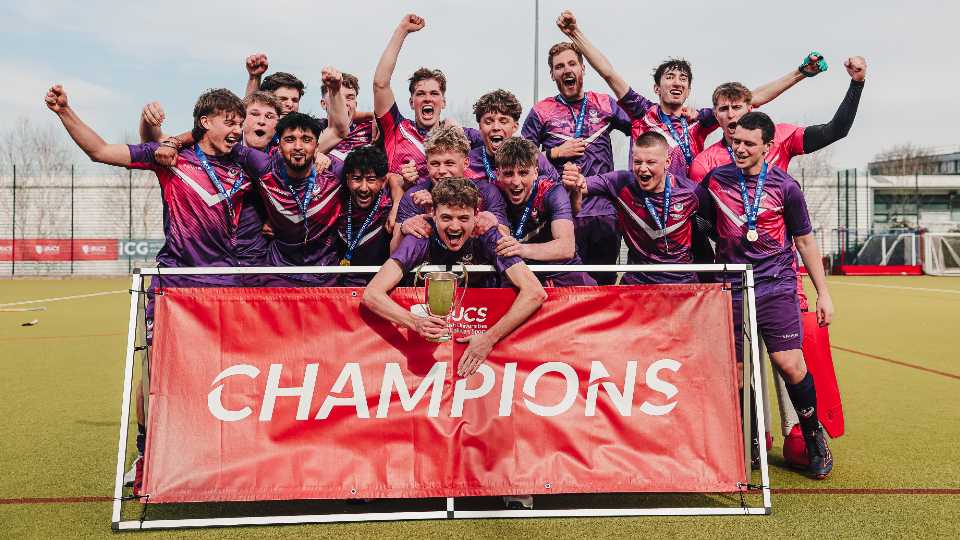 A Loughborough sports team wearing medals and holding a trophy, celebrating behind a BUCS champions banner.