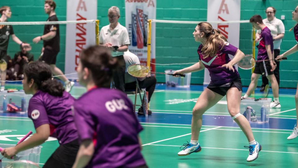 Student playing badminton on an indoor court.