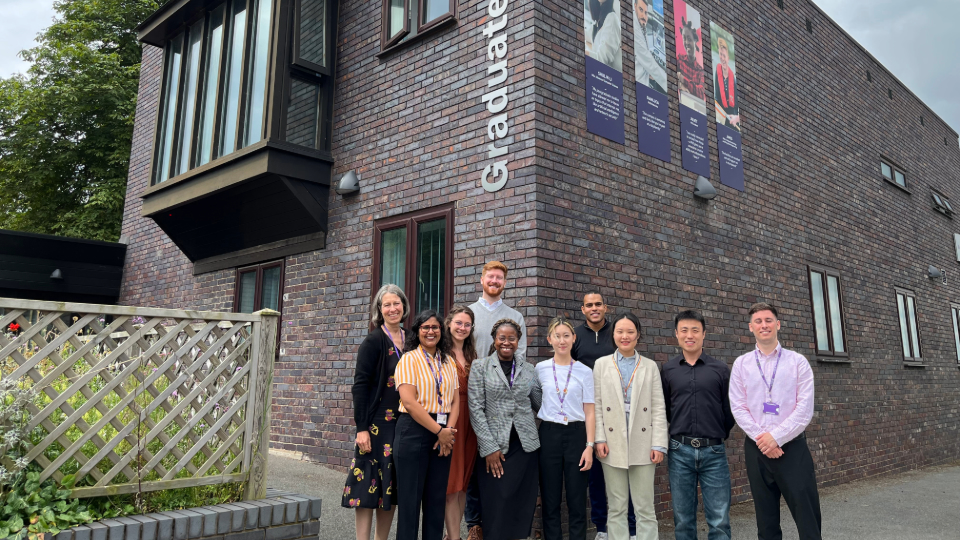 Some Loughborough University doctoral innovation consultants stood beside their supporting staff in front of the Graduate House building