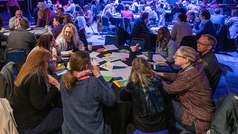 A group of colleagues sat at a roundtable talking and listening to each other.
