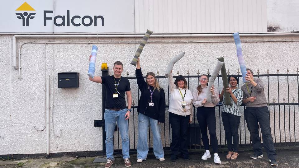 Six people standing outside the Falcon Centre holding handmade draft excluders.