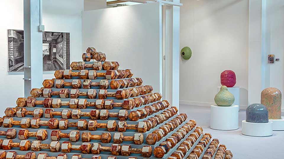 A pyramid of ceramic dumbbells alongside other sculptures in a gallery.