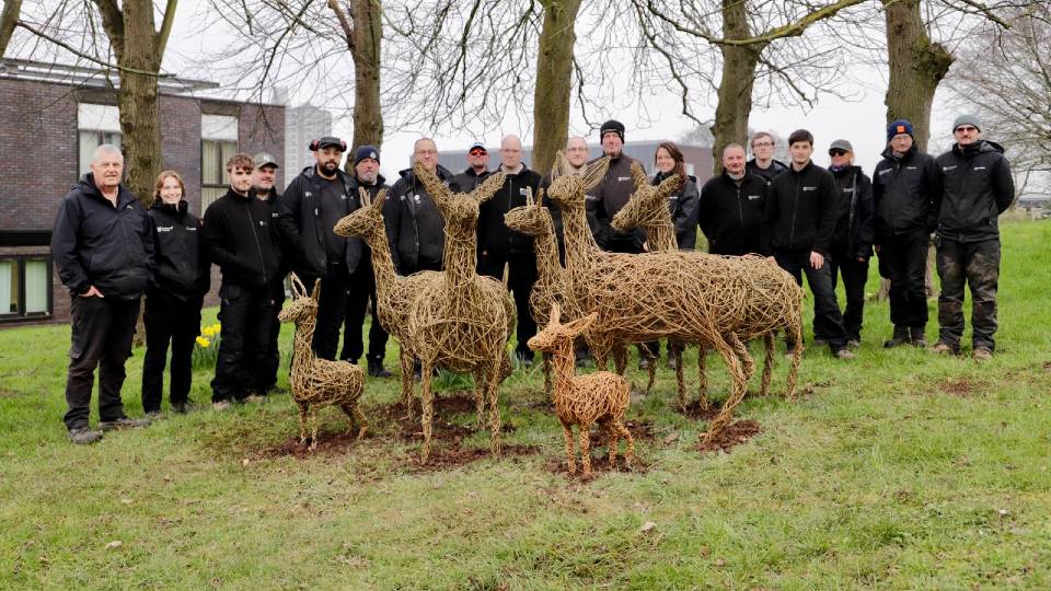 The University Gardens team standing with a group of handcrafted willow deer on campus.