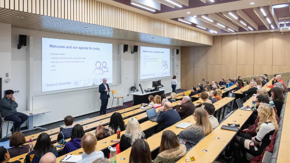 Attendees sat listening to the Vice-Chancellor as he presents at the front of a lecture theatre