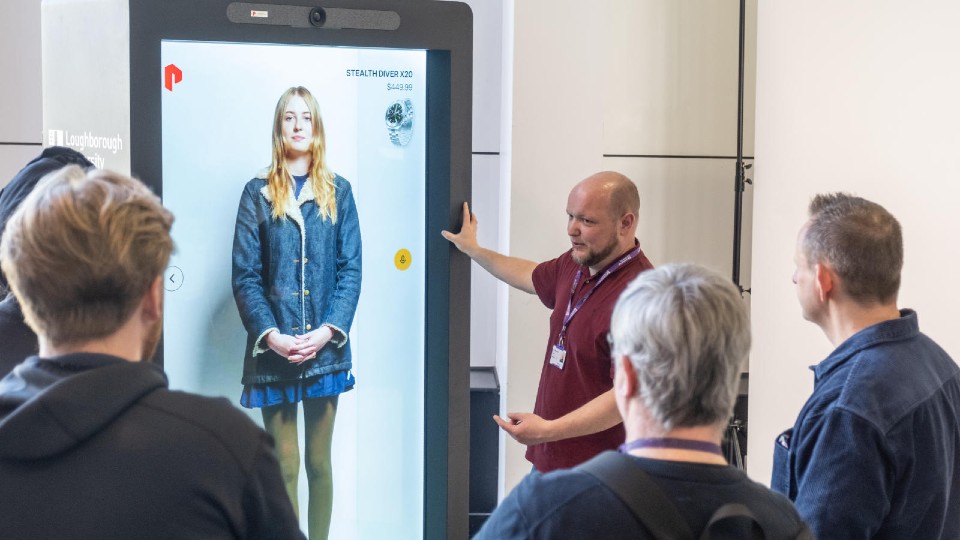 A group of people looking at a hologram box, with a student standing in it.