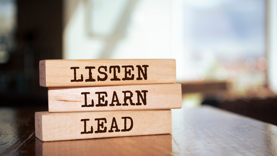 Three wooden blocks on a table with the words 'listen, learn and lead' written on them.