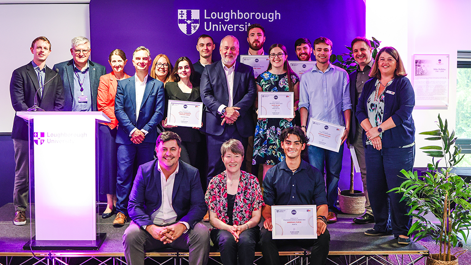 Photo of a group of winners from the evening stood on stage together with their certificates smiling at the camera, along with University staff including the Vice Chancellor