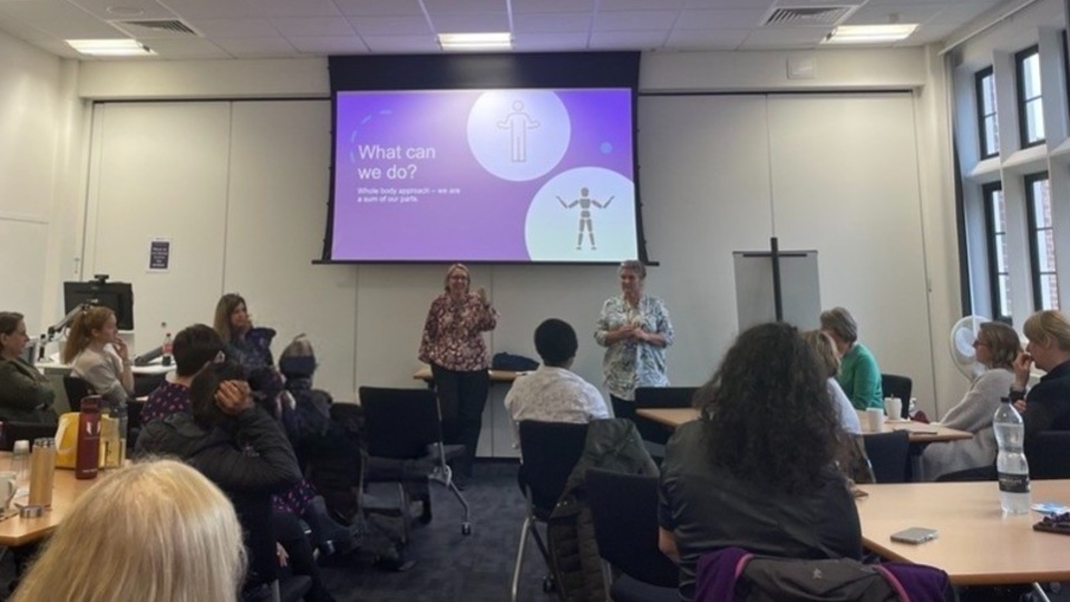 Members of staff sitting around tables listening to a presentation at the Menopause Café.