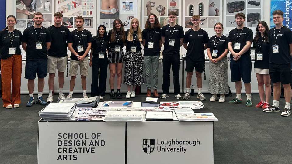 A group of students standing in a row in front of their work at the New Designers exhibition.