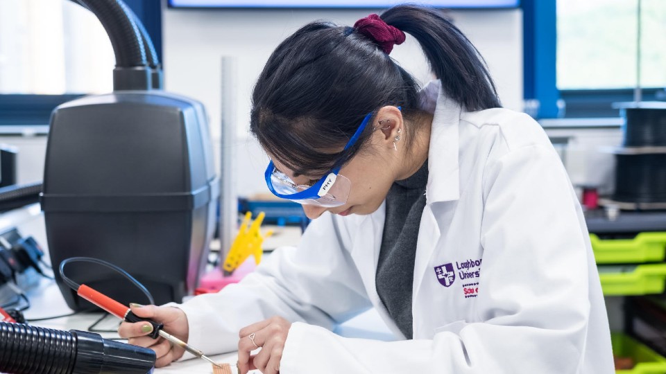 A physics student holding a screwdriver and wearing protecting glasses whilst working.