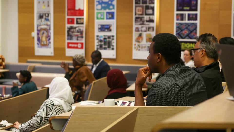 Attendees of the conference sat down in a lecture theatre facing towards a speaker at the front of the room