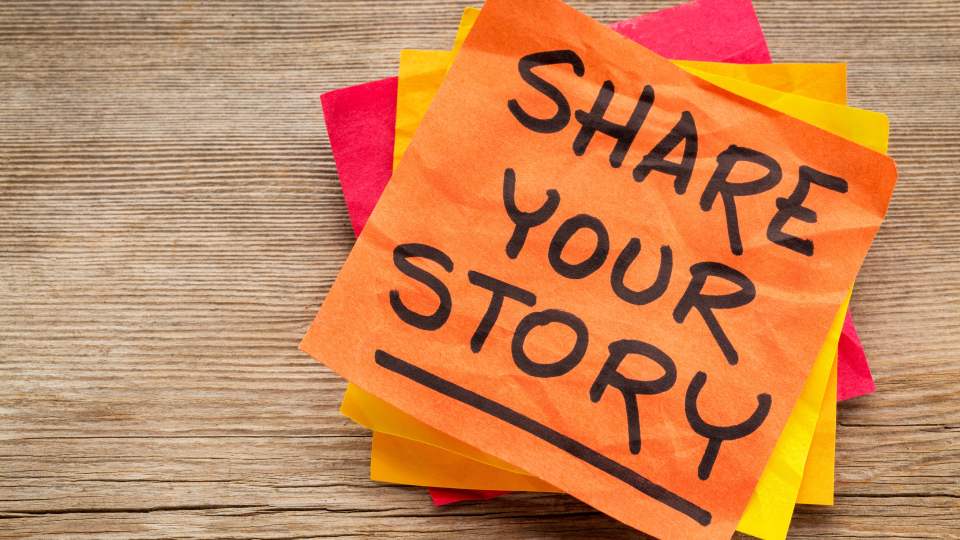 A stack of a post-it notes on a wooden surface, 'share your story' is written on the top note.