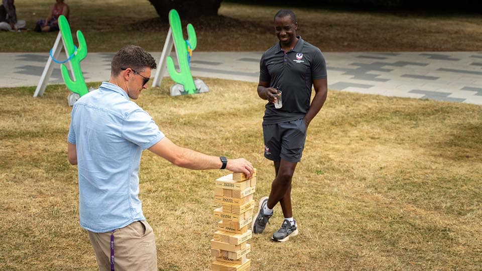 Two people playing giant Jenga outside at the staff summer picnic.