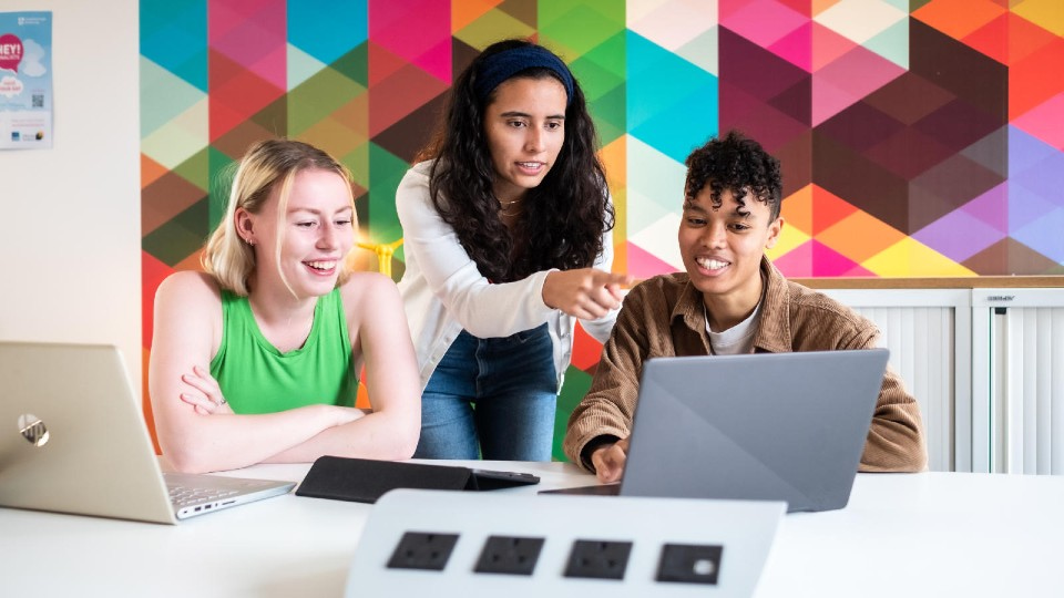 Three students working together on a laptop at a table.