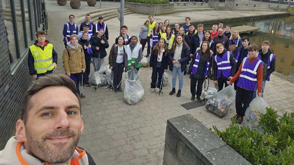 A group of Loughborough staff and students standing outdoors holding bags of rubbish and litter picker tools.