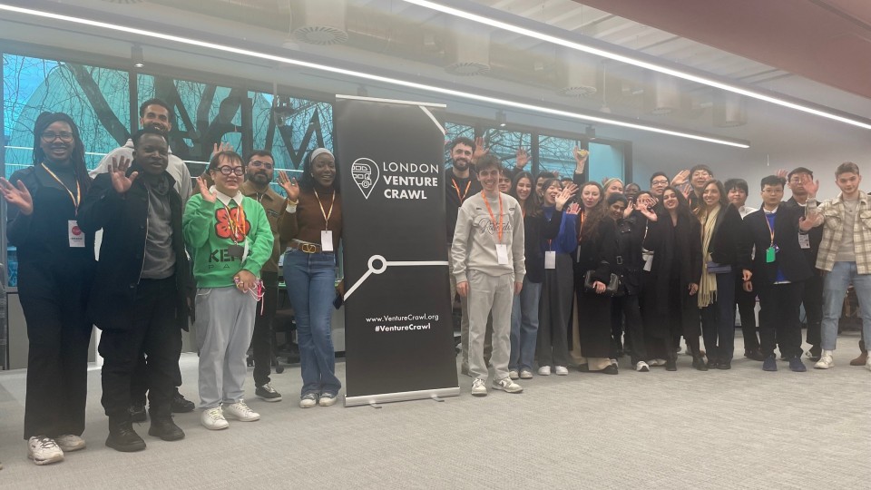 A group of students standing next to a sign waving.